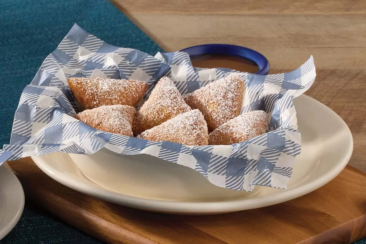 Cracker Barrel's Biscuit Beignets dusted with powdered sugar and served with a sweet dipping sauce.