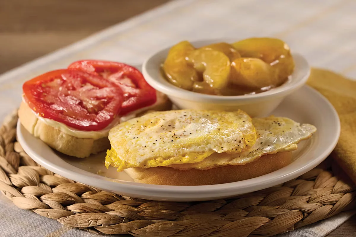Cracker Barrel's Egg Sandwich with fluffy scrambled eggs on toasted bread, served with a side of crispy bacon or sausage.