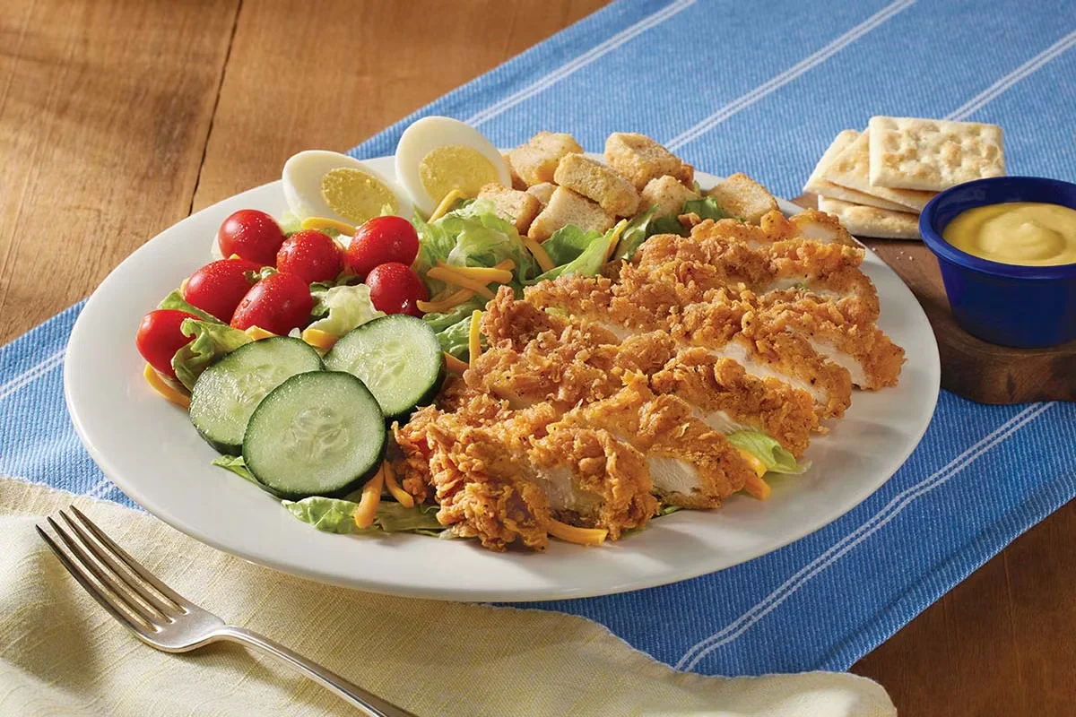 Cracker Barrel's Homestyle Fried Chicken Salad, featuring crispy fried chicken on fresh greens with tomatoes, cucumbers, shredded cheese, and croutons.