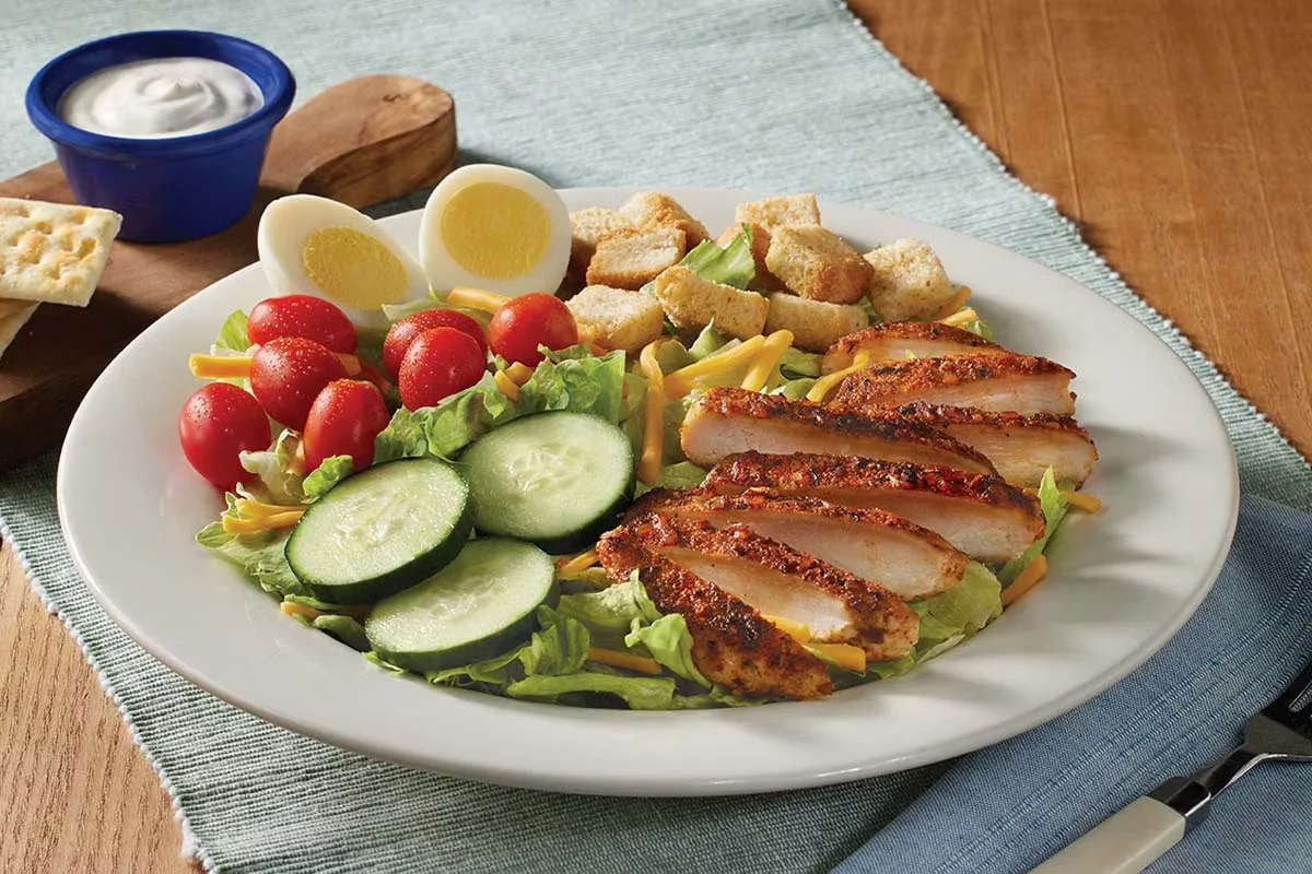 Cracker Barrel's Homestyle Grilled Chicken Salad, featuring tender grilled chicken on fresh greens with tomatoes, cucumbers, shredded cheese, and croutons.