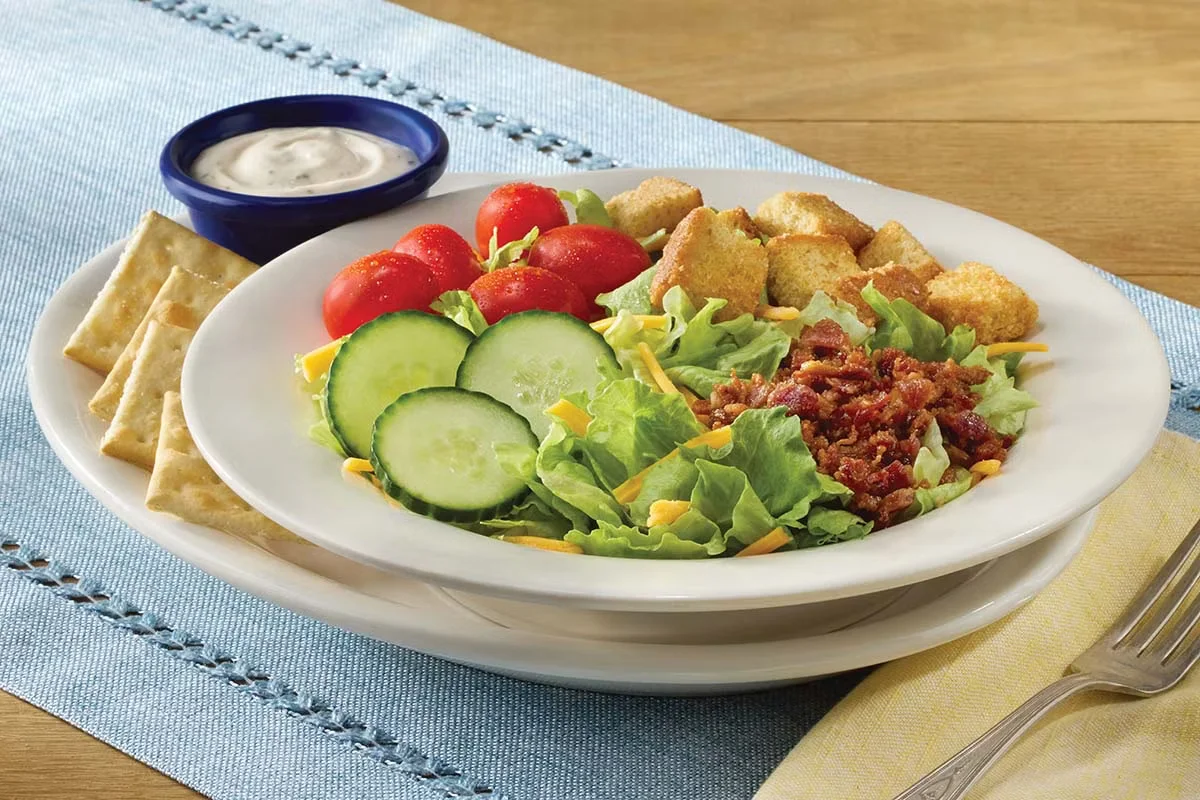 Cracker Barrel's House Salad, featuring fresh greens, tomatoes, cucumbers, shredded cheese, and croutons, served with your choice of dressing.