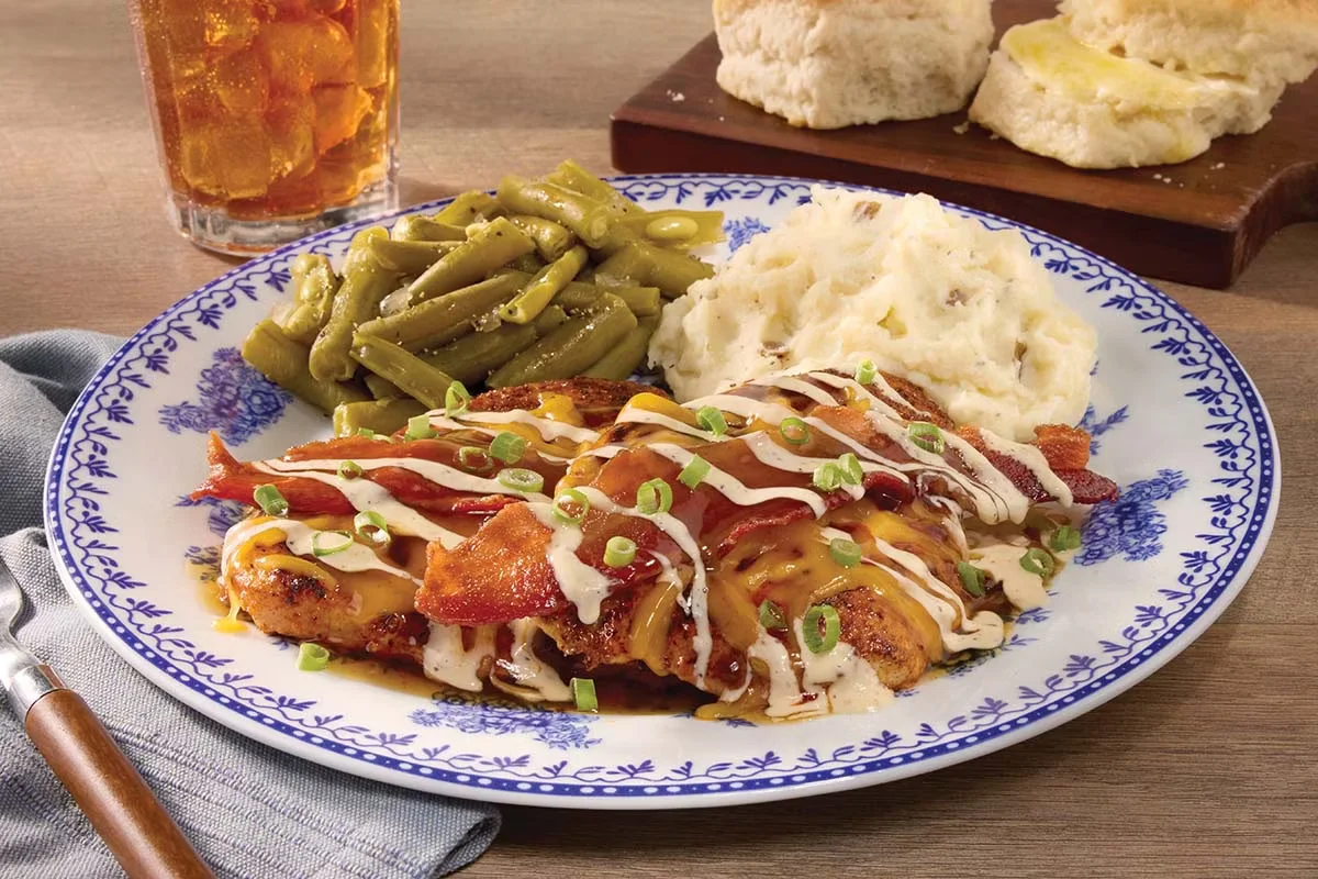 Cracker Barrel's Maple Bacon Grilled Chicken topped with crispy bacon, melted cheese, and a sweet maple glaze, served with sides.